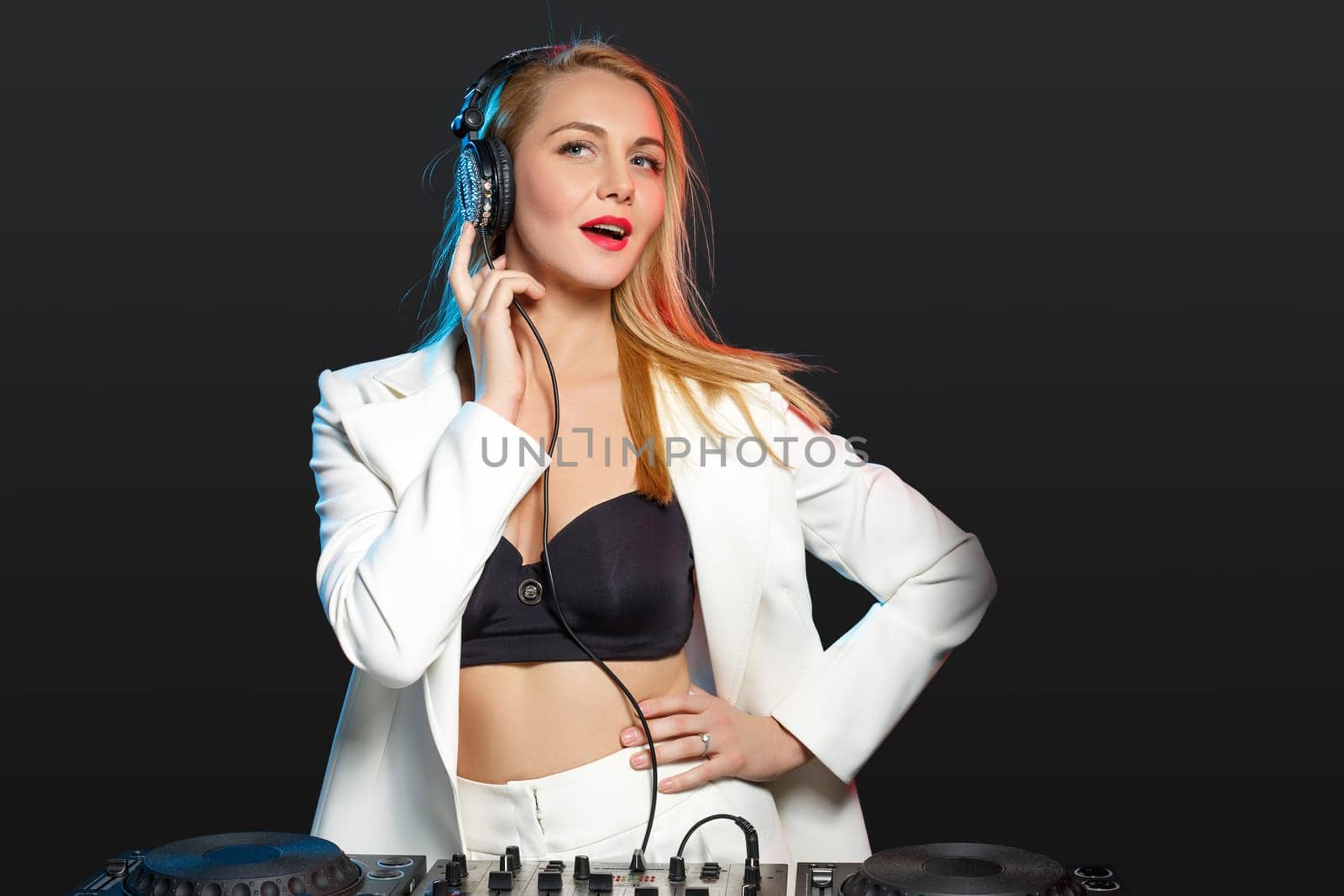 Beautiful blonde DJ girl in a white suit on decks on the party on the black background