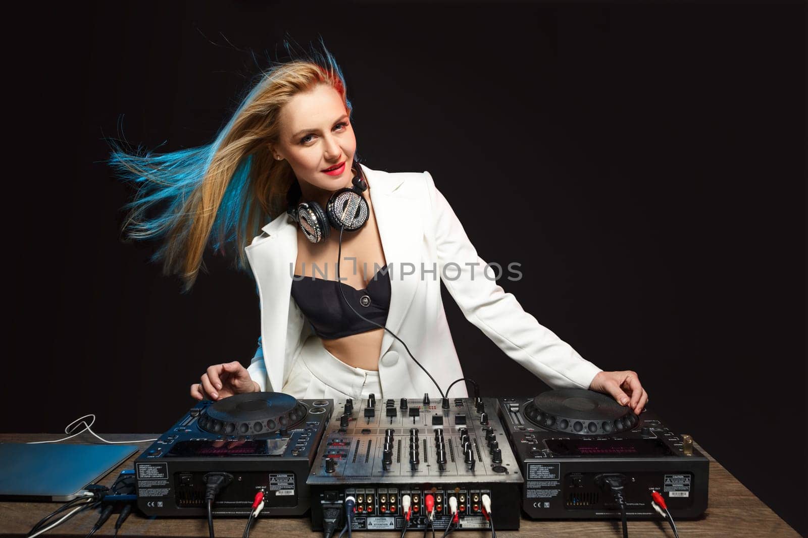 Beautiful blonde DJ girl in a white suit on decks on the party on the black background