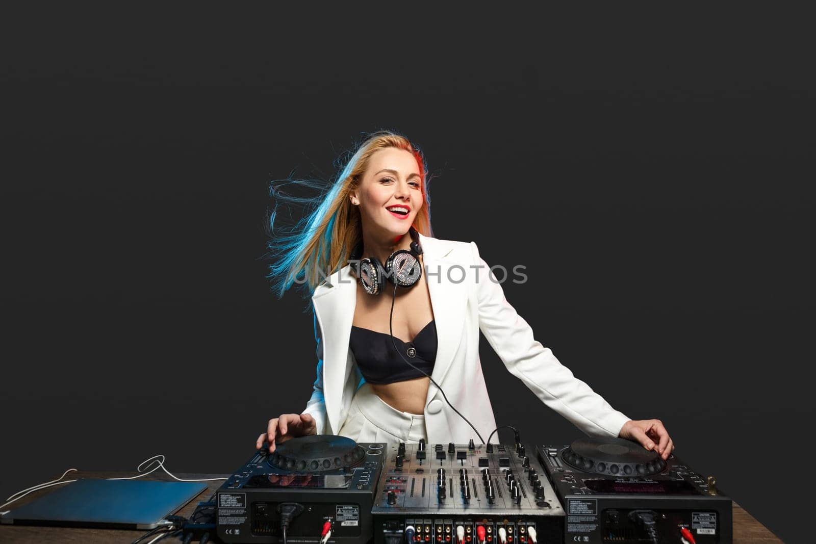 Beautiful blonde DJ girl in a white suit on decks on the party on the black background