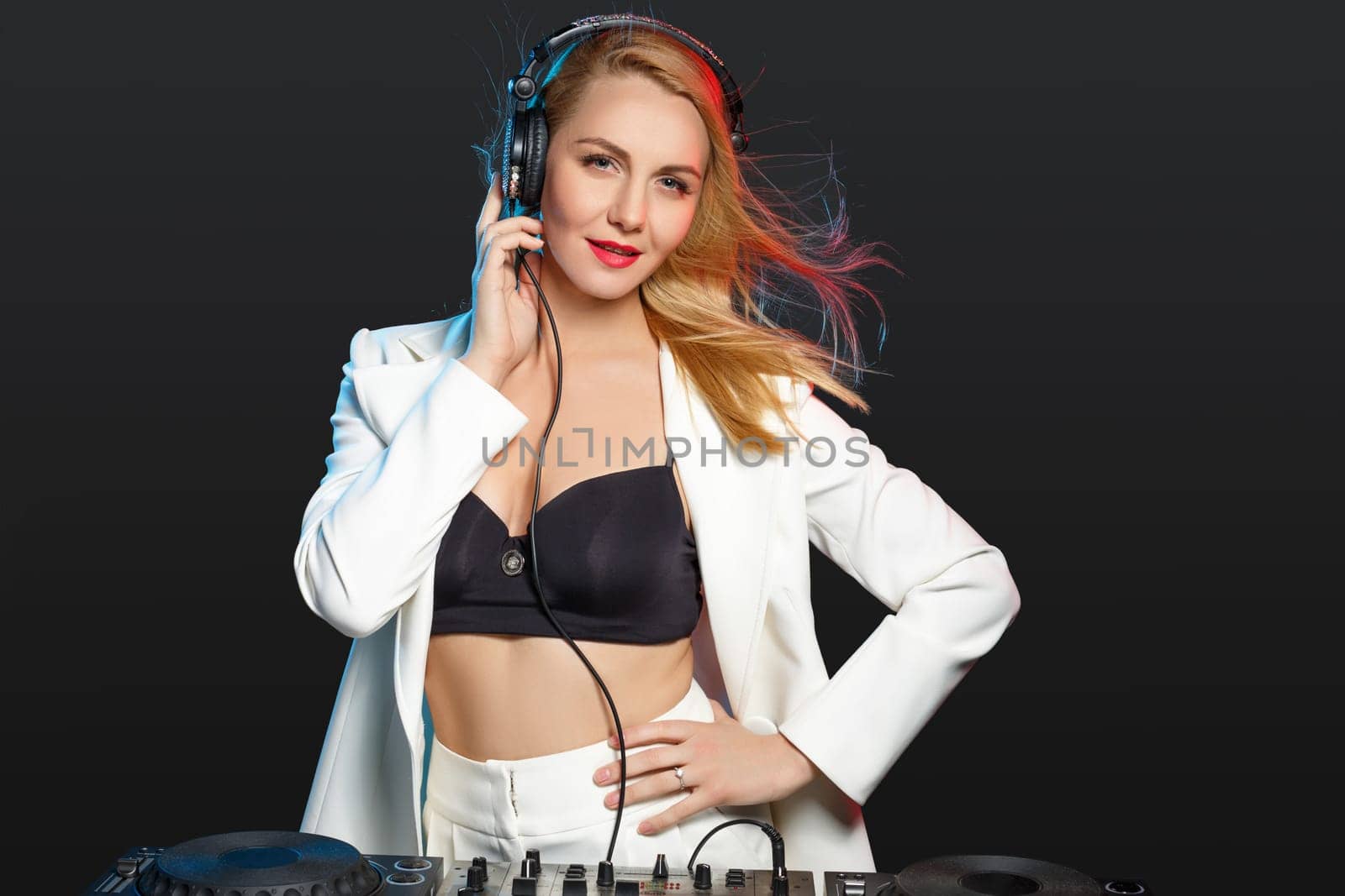 Beautiful blonde DJ girl in a white suit on decks on the party on the black background