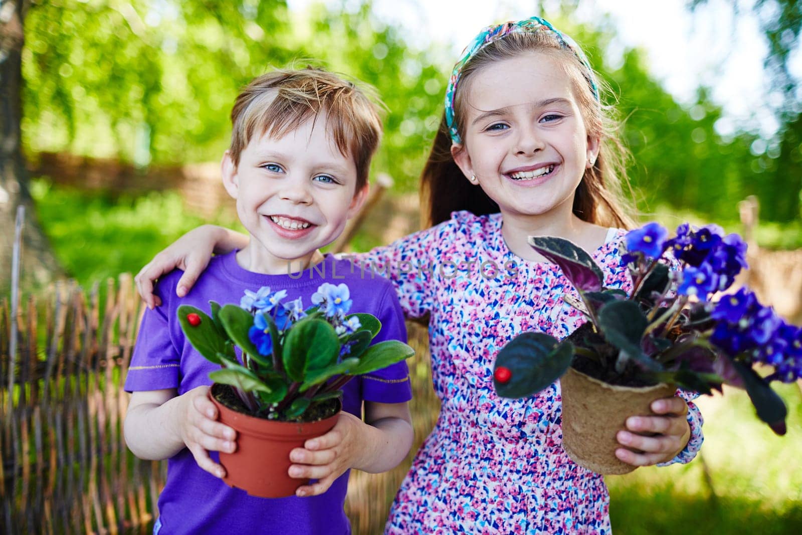 Friendly boy and girl with garden violets looking at camera in natural environment
