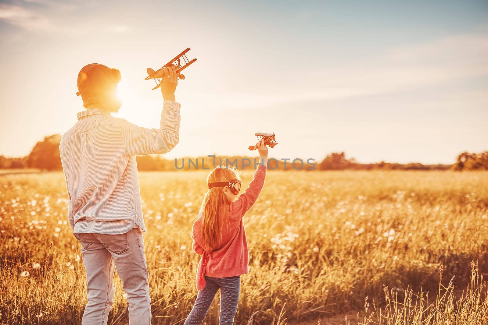Father with his child playing with toy of plane on the evening field. Concept of love and family vacation.