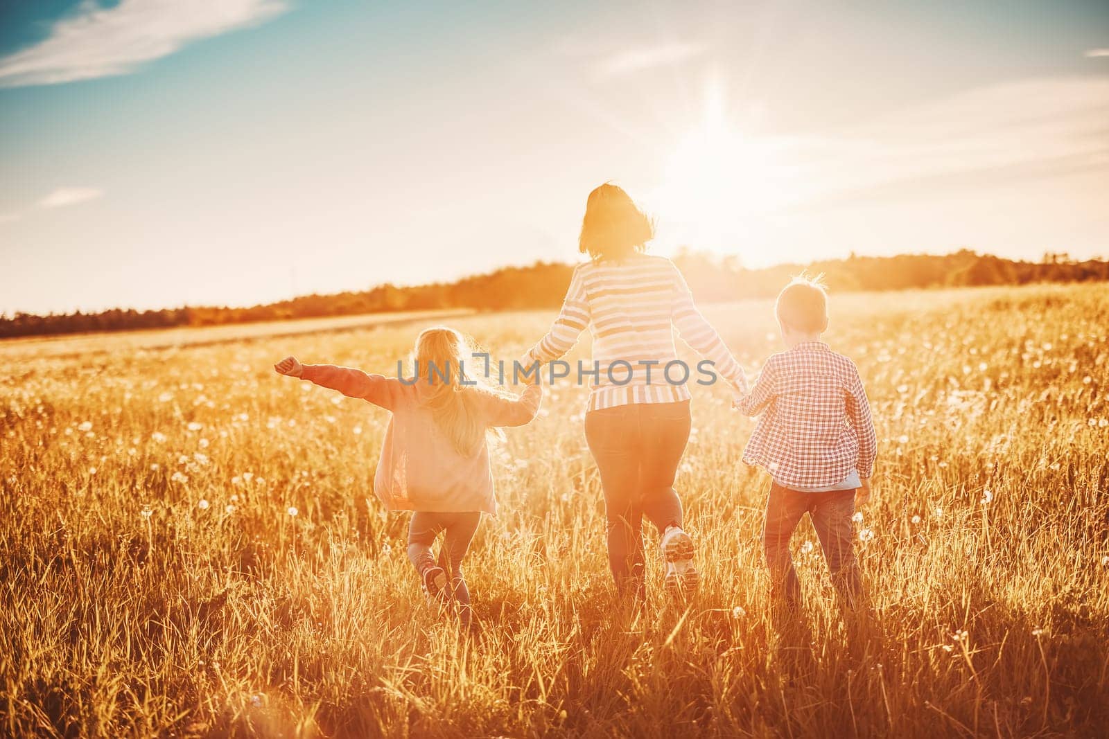 Mother with her children running on the field on the summer sunset. Concept of the family relationship and vacation.