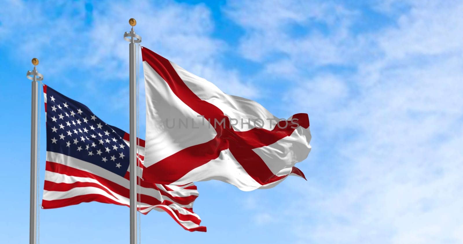 The flag of the state of Alabama waving alongside the national flag of the United States on a sunny day. The flag of Alabama features a red cross on a white field. Realistic 3d illustration