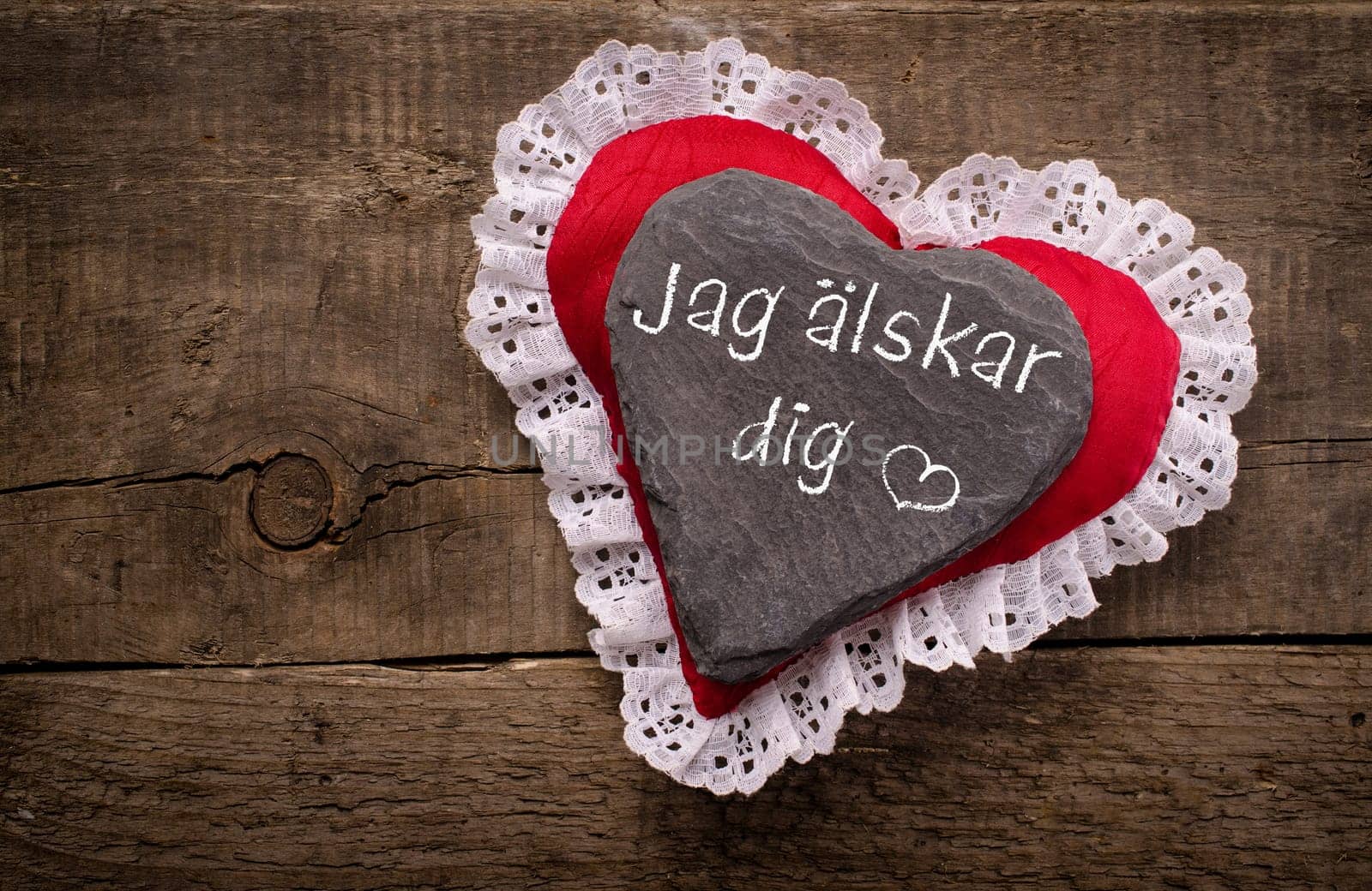 Heart shape of dark slate with the Swedish inscription Jag älskar dig, I love you, on a red fabric heart shape