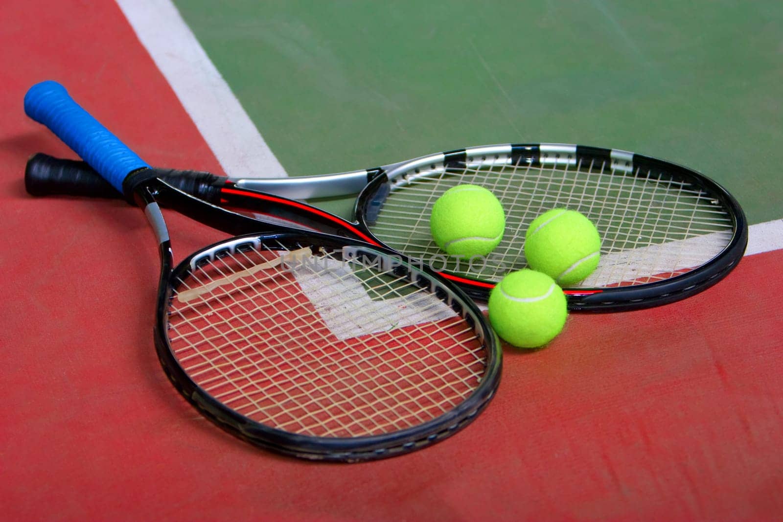 Two tennis racket and three balls on the indoor court.