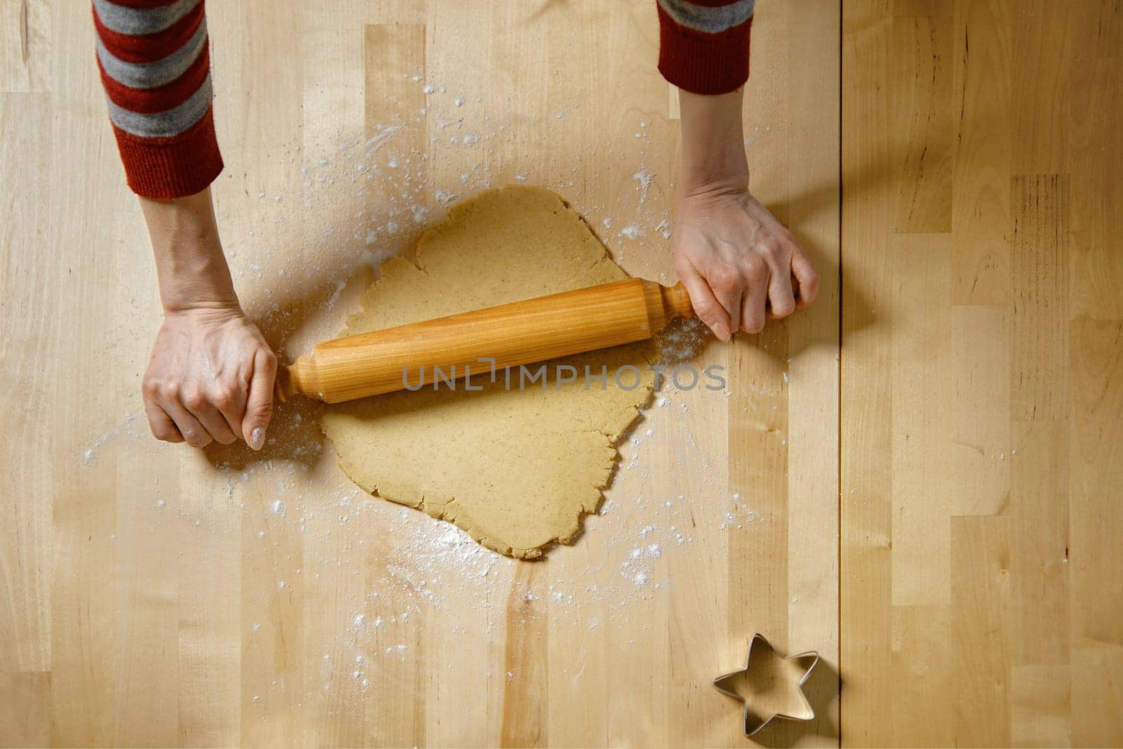Top view at unrecognizable woman rolling out dough with rolling pin. A woman makes ginger cookies at home.