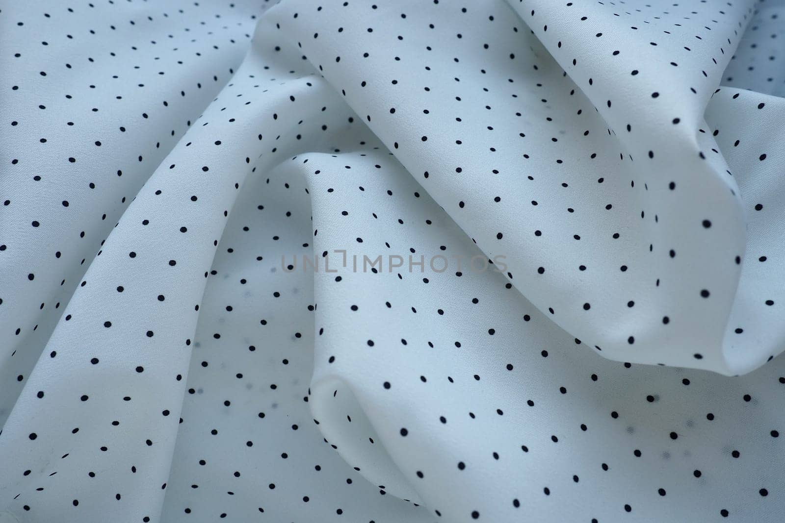 Texture of silk fabric. Black polka dots on a white background. Dress lightweight synthetic fabric in white with a repeating pattern. The textile is made up of waves and folds. Feminine classic style