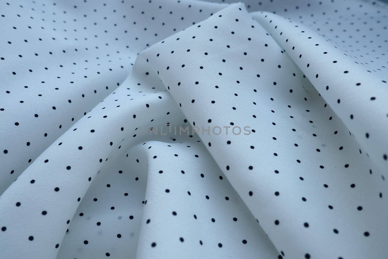 Texture of silk fabric. Black polka dots on a white background. Dress lightweight synthetic fabric in white with a repeating pattern. The textile is made up of waves and folds. Feminine classic style