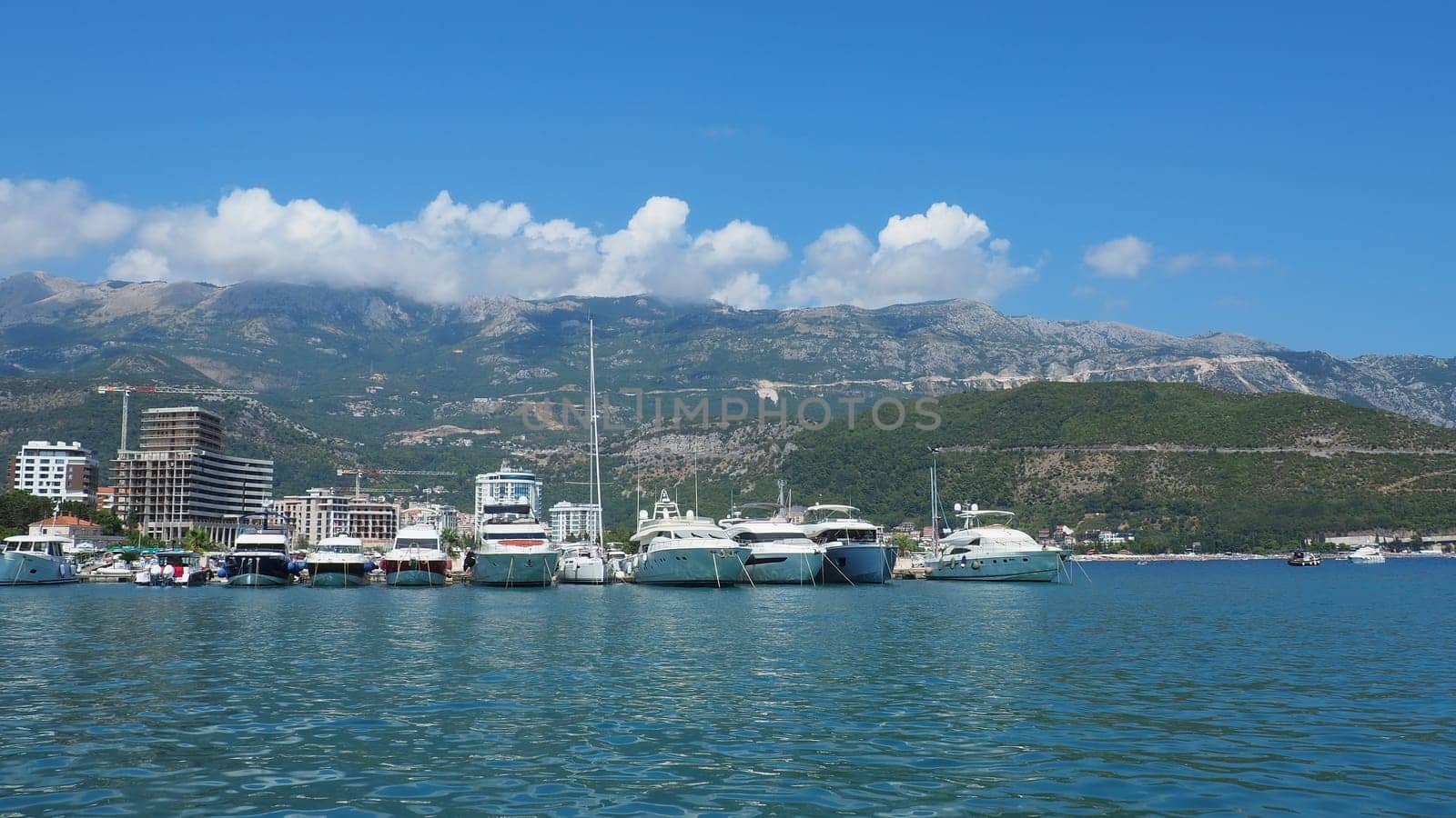 Budva, Montenegro, August 15 2022 Adriatic sea, coast, mountains, sea ripples. Boats and ships are moored to the embankment. Water transport parking. Summer resort trips with tourist water activities.