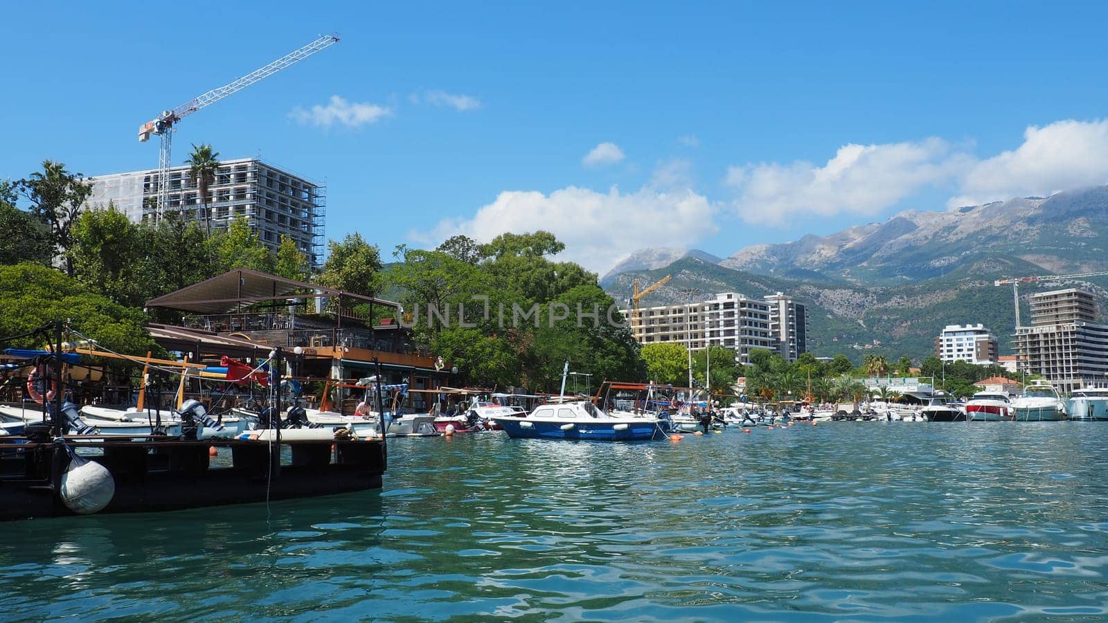 Budva, Montenegro, August 15 2022 Adriatic sea, coast, mountains, sea ripples. Boats and ships are moored to the embankment. Water transport parking. Summer resort trips with tourist water activities.