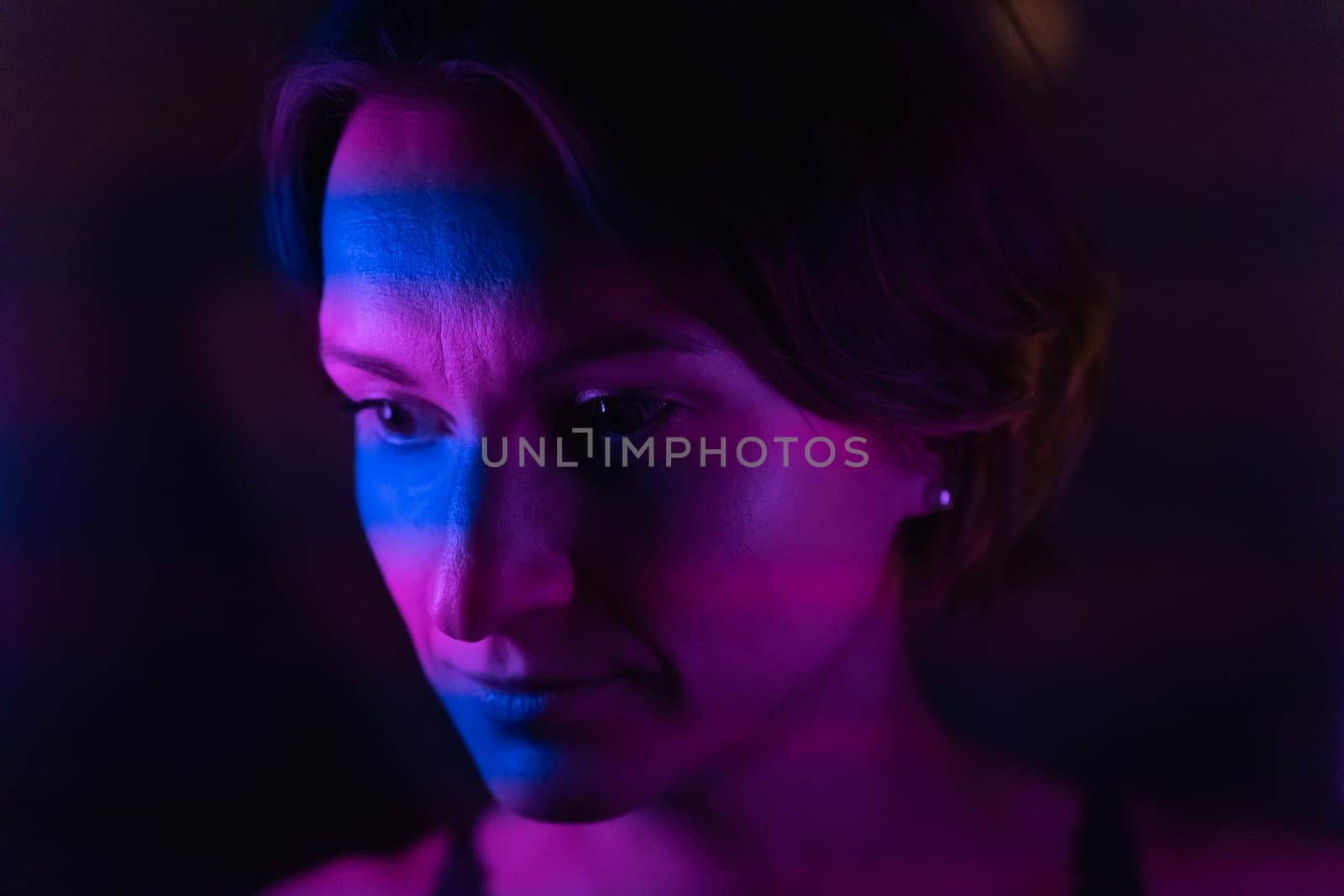Stripes of blue and purple or purple neon light up the face of a young dark-haired woman.
