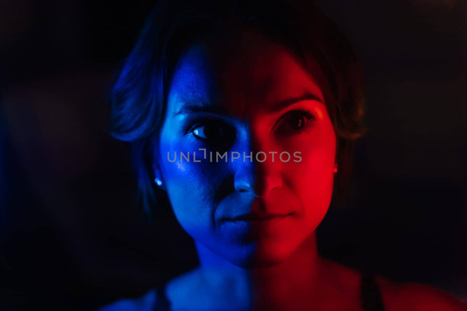 The face of a young woman in blue and red neon light on a dark background.