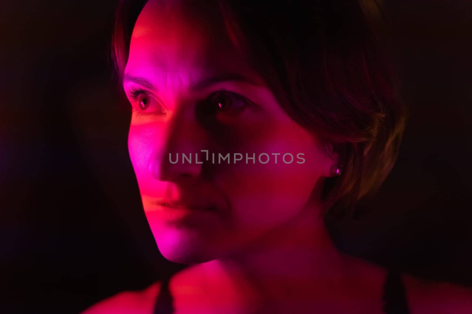 Close-up portrait of a young woman illuminated by stripes of pink and red.