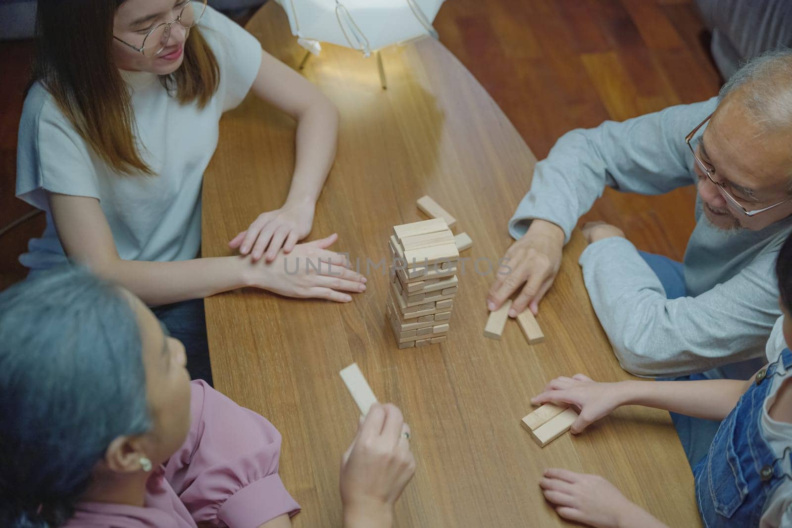 Happy grandparents Asian family enjoy playing toy block with little daughter together in home living room at night time, Smiling parent having fun play build constructor tower of wooden blocks