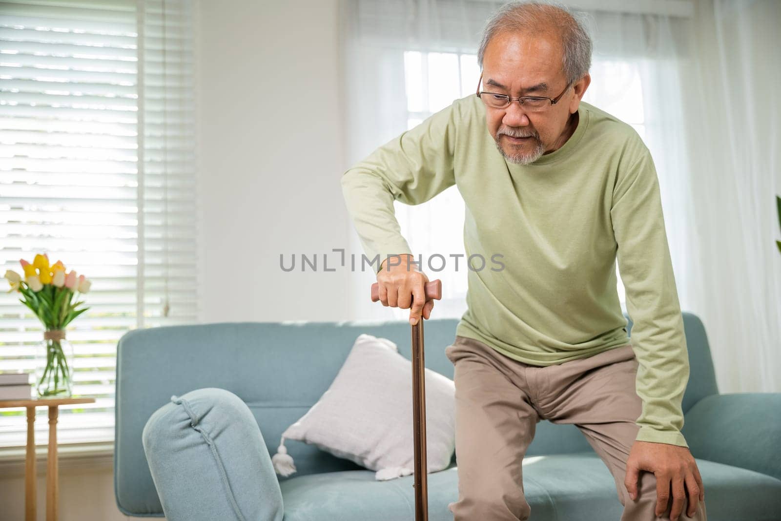 Asian Old man with eyeglasses typing to stand up from sofa with walking cane, Elderly suffering from knee pain ache holding handle of cane, senior disabled man holding walking stick at home