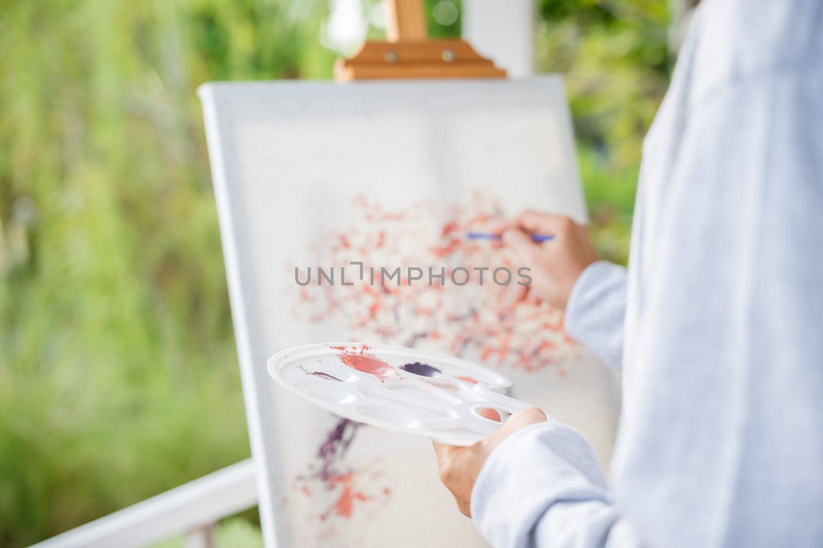 Lifestyle artist. Senior old man painting picture artwork using brush and water color on canvas, portrait elderly white haired paint at his easel outside green nature, Happy retirement and activity