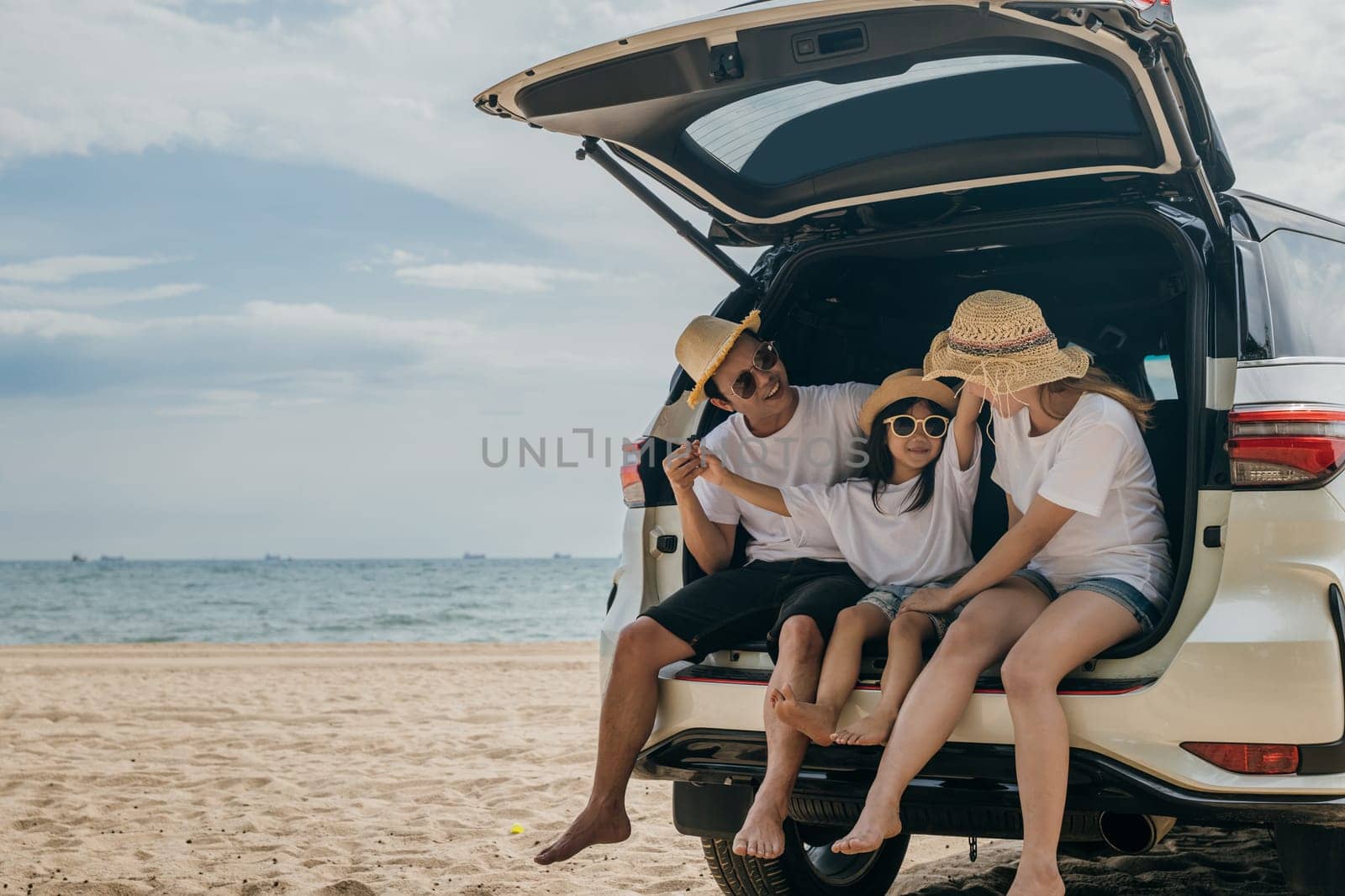 Happy Family Day. Dad, mom and daughter enjoying road trip sitting on back car, Parents and children traveling in holiday at sea beach, family having fun in summer vacation on beach with automobile