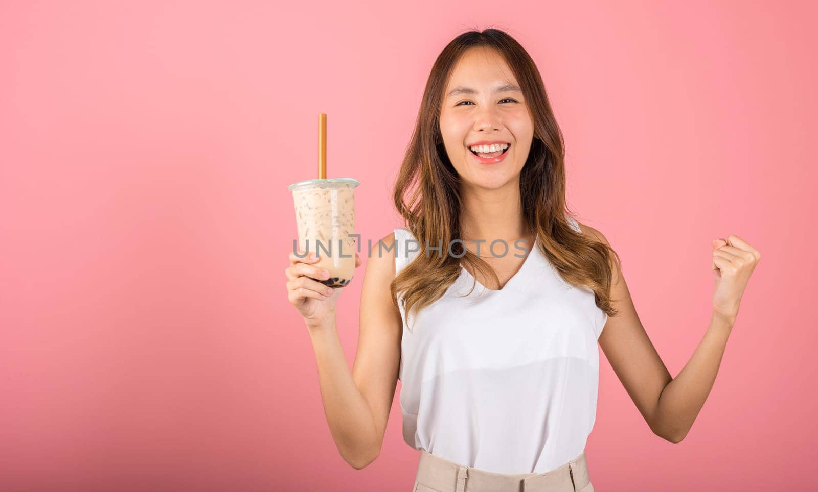 Excited Asian beautiful woman holding drinking brown sugar flavored tapioca pearl bubble milk tea, Happy smiling portrait female success, isolated on pink background, pearl milk tea beverage concept