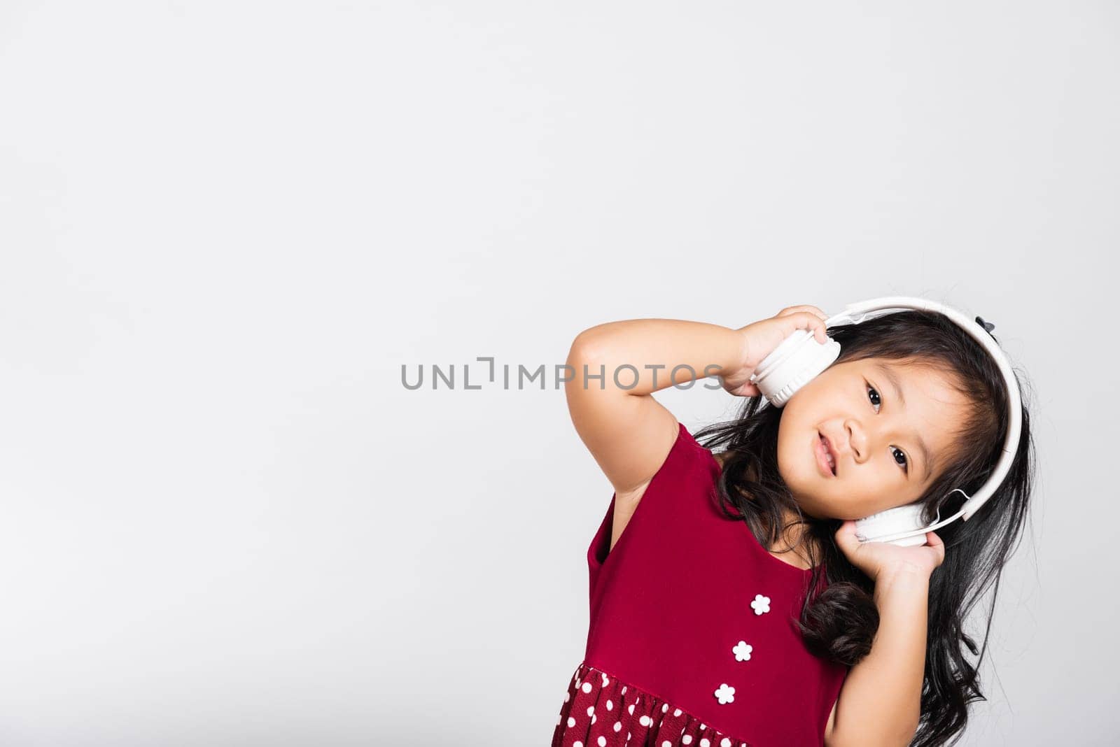 Little cute kid girl 3-4 years old listen music in wireless headphones in studio shot isolated on white background, happy Asian children smiling listening audio, entertainment lifestyle