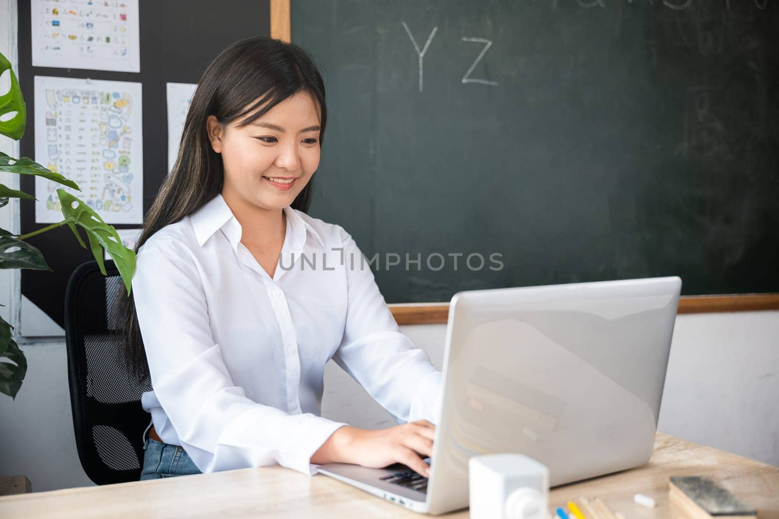 Back to school. Smiling female using computer sitting at school table, Portrait of young woman teacher with laptop at desk in classroom, Online education and learning concept