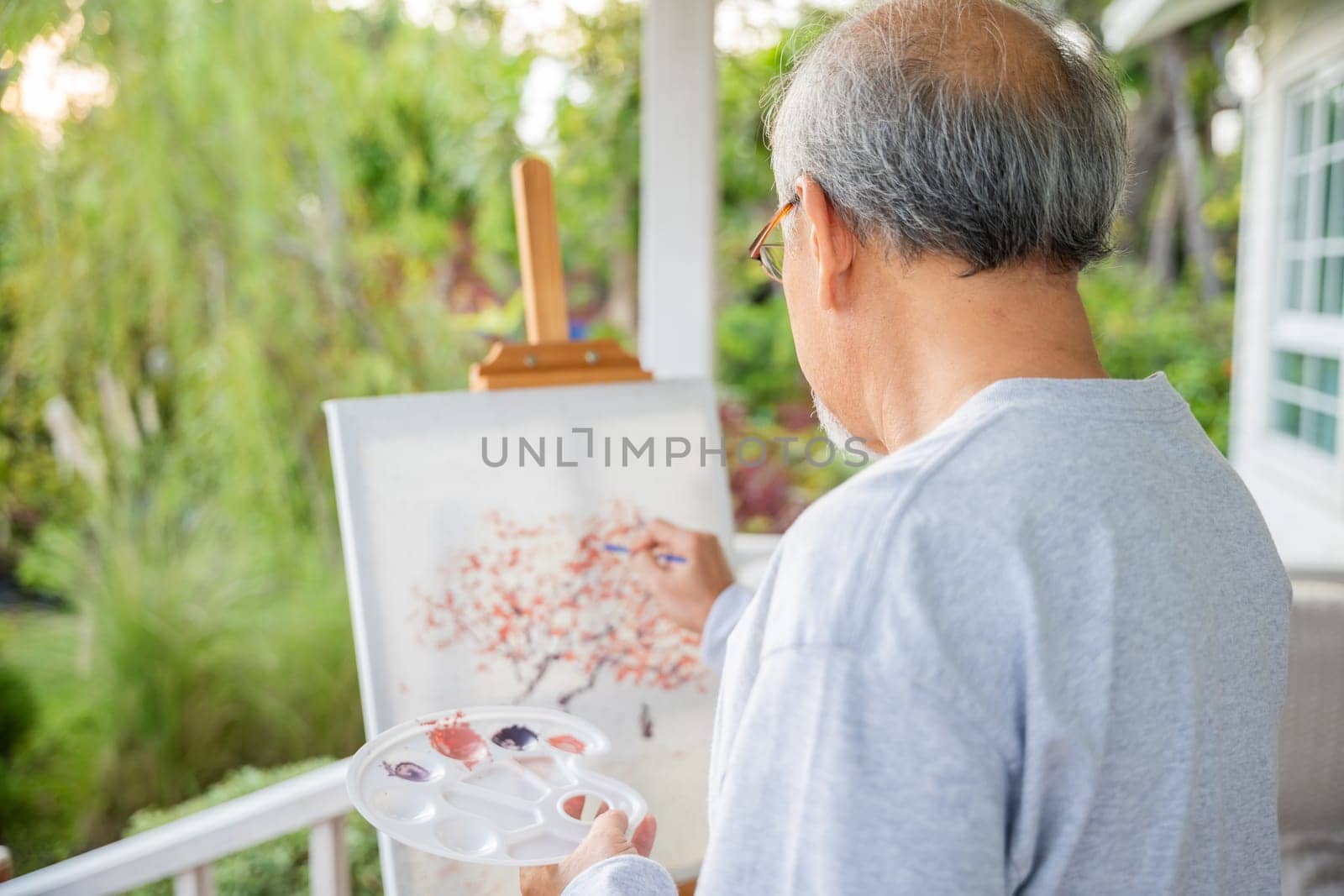 Lifestyle Asian senior old man painting picture artwork using brush and oil color on canvas, elderly people smile paint at his easel outside green nature background, Happy retirement artist activity