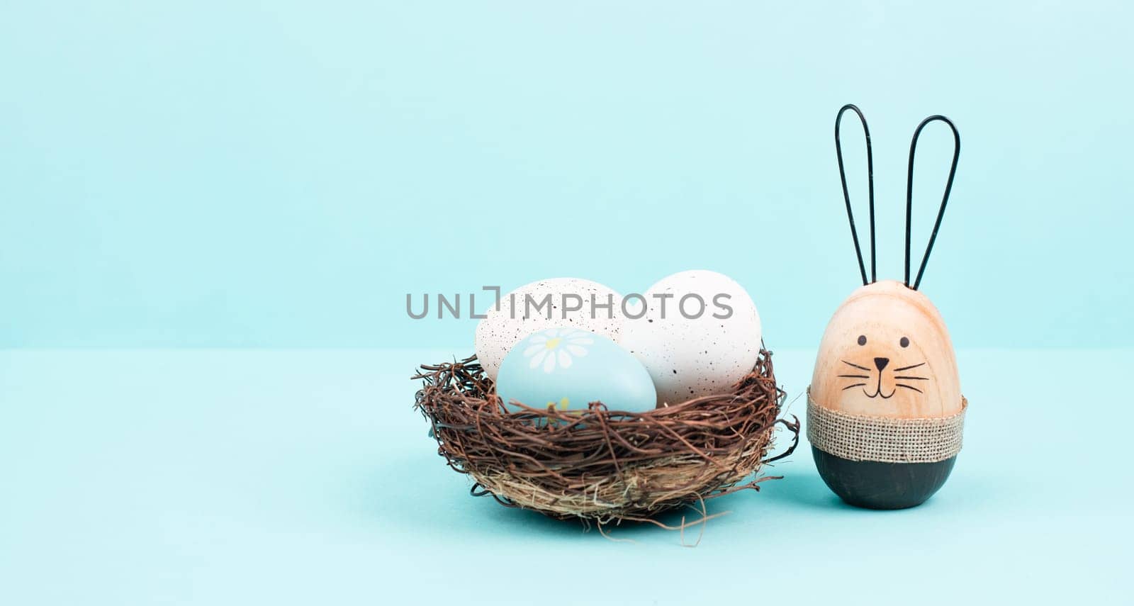 Easter bunny or rabbit sitting nest to a wicker nest filled with colorful eggs, spring holiday