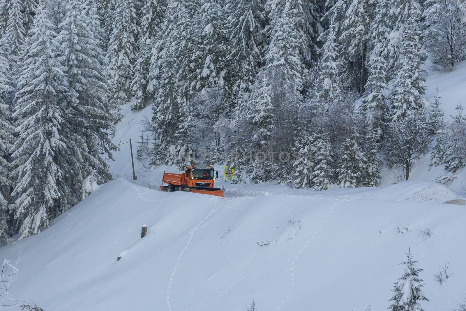 Snow plow truck cleaning snowy road in snowstorm. Snowfall on the driveway.