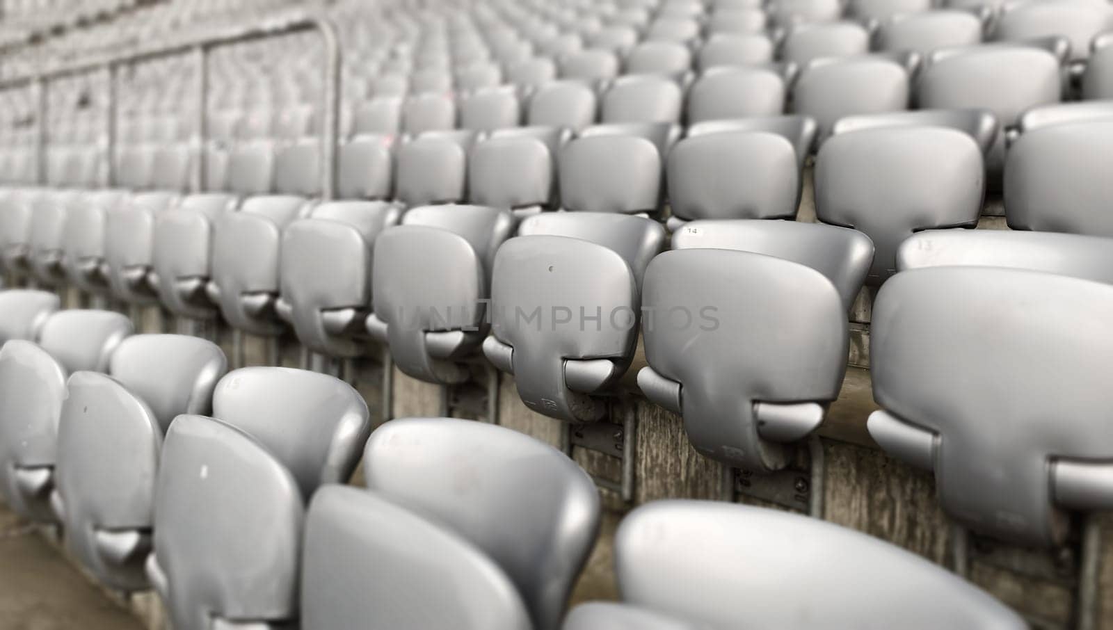Empty gray chairs inside a stadium. Plastic seats arranged in rows. Repetition and symmetry.