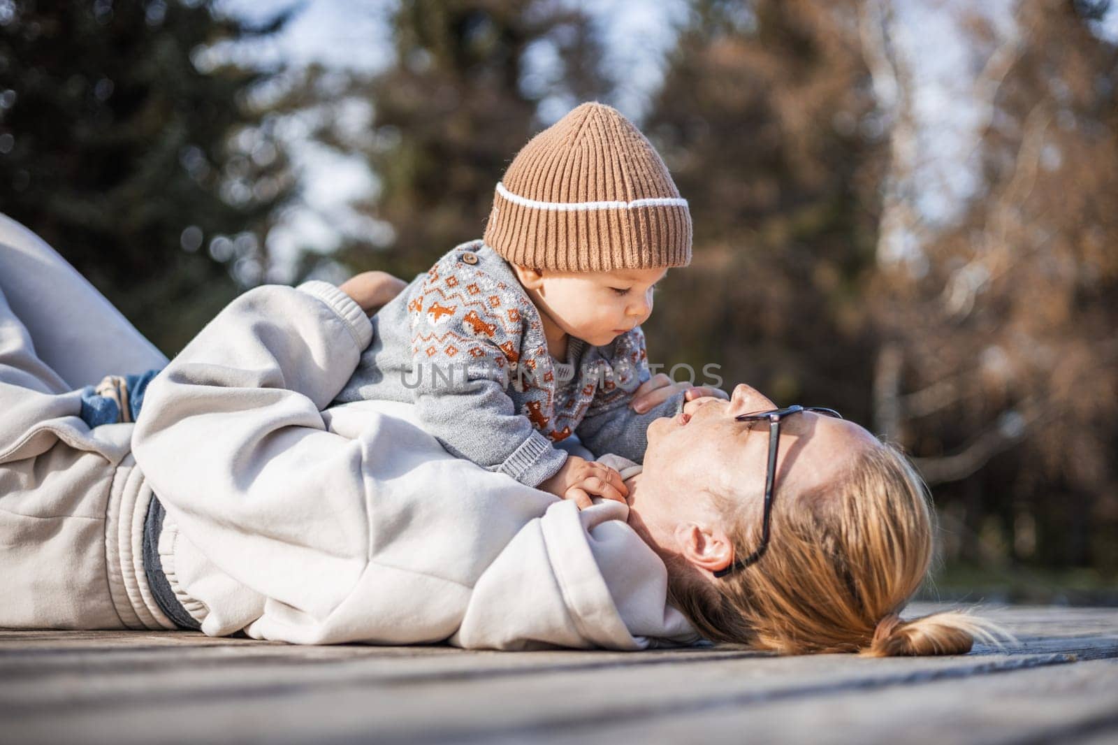 Happy family. Young mother playing with her baby boy infant oudoors on sunny autumn day. Portrait of mom and little son on wooden platform by lake. Positive human emotions, feelings, joy