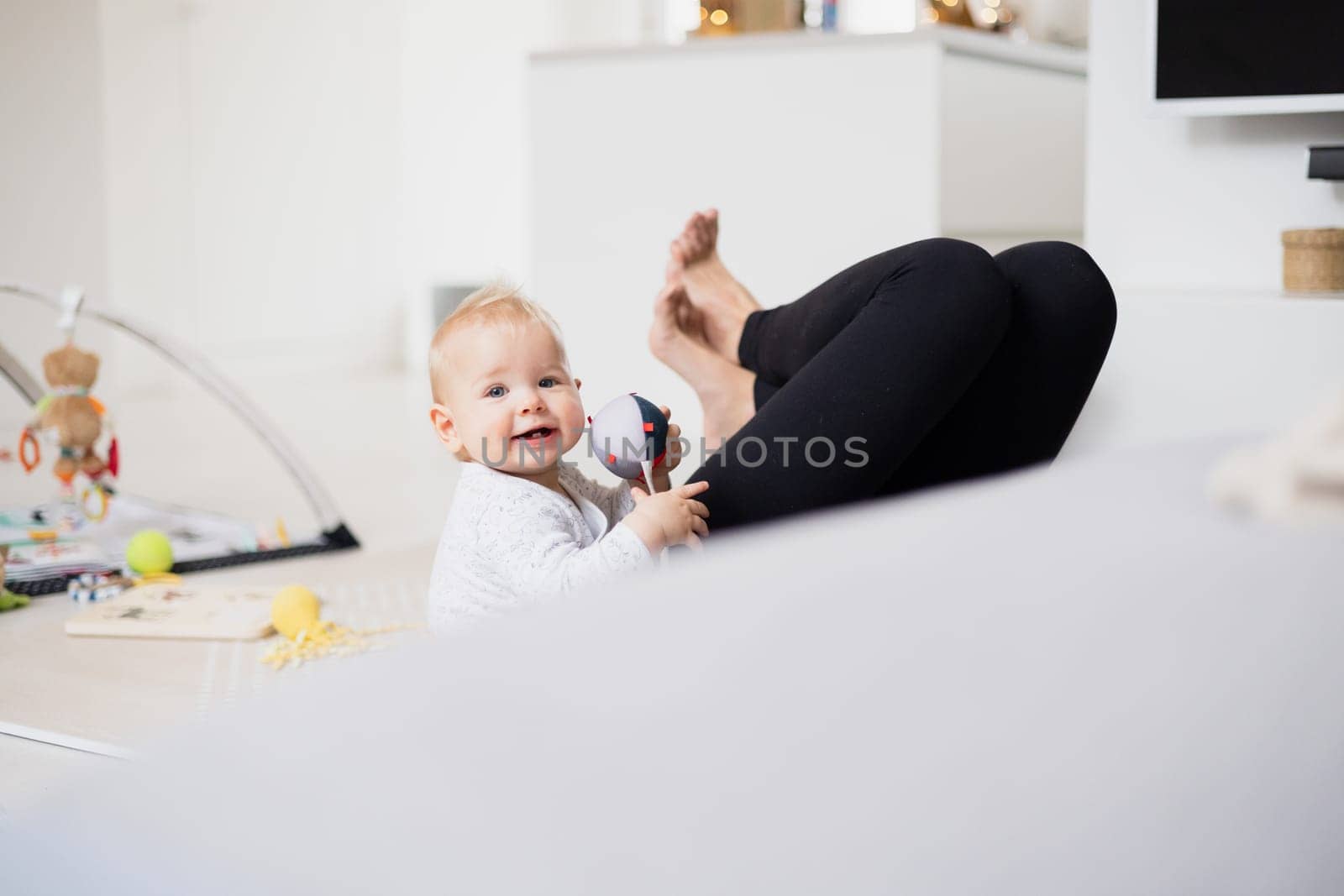 Happy family moments. Mother lying comfortably on children's mat playing with her baby boy watching and suppervising his first steps. Positive human emotions, feelings, joy