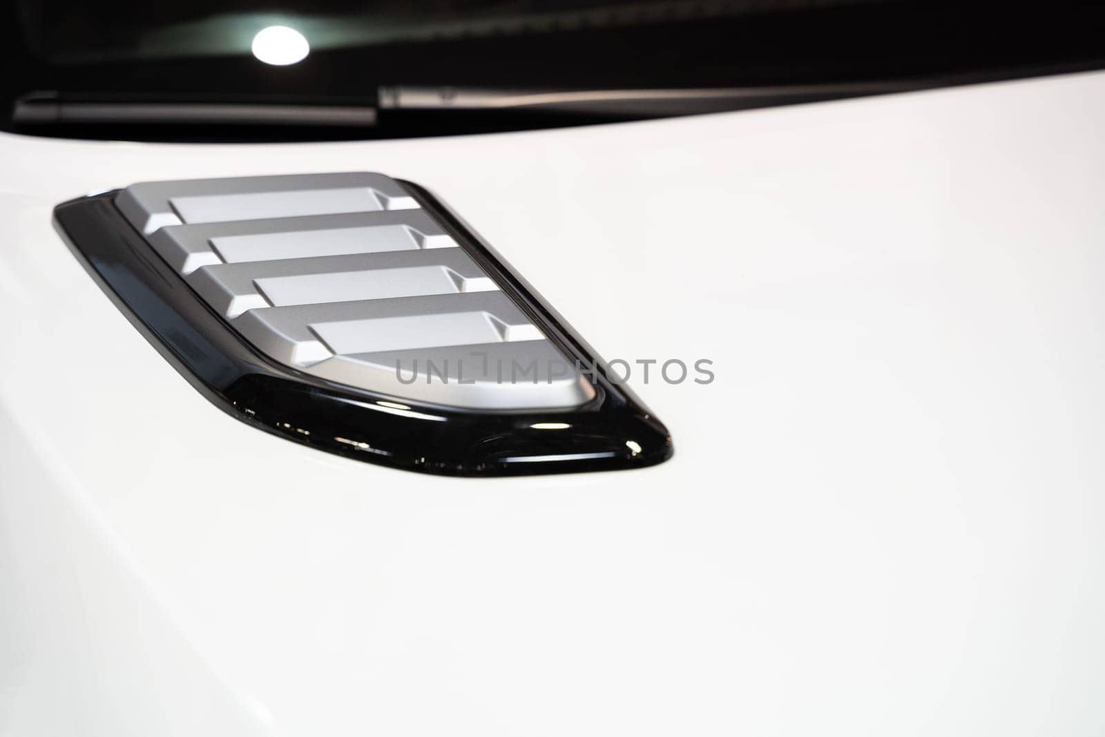 front view closeup detail of sport car with white metal hood and grey air flow intake ornament