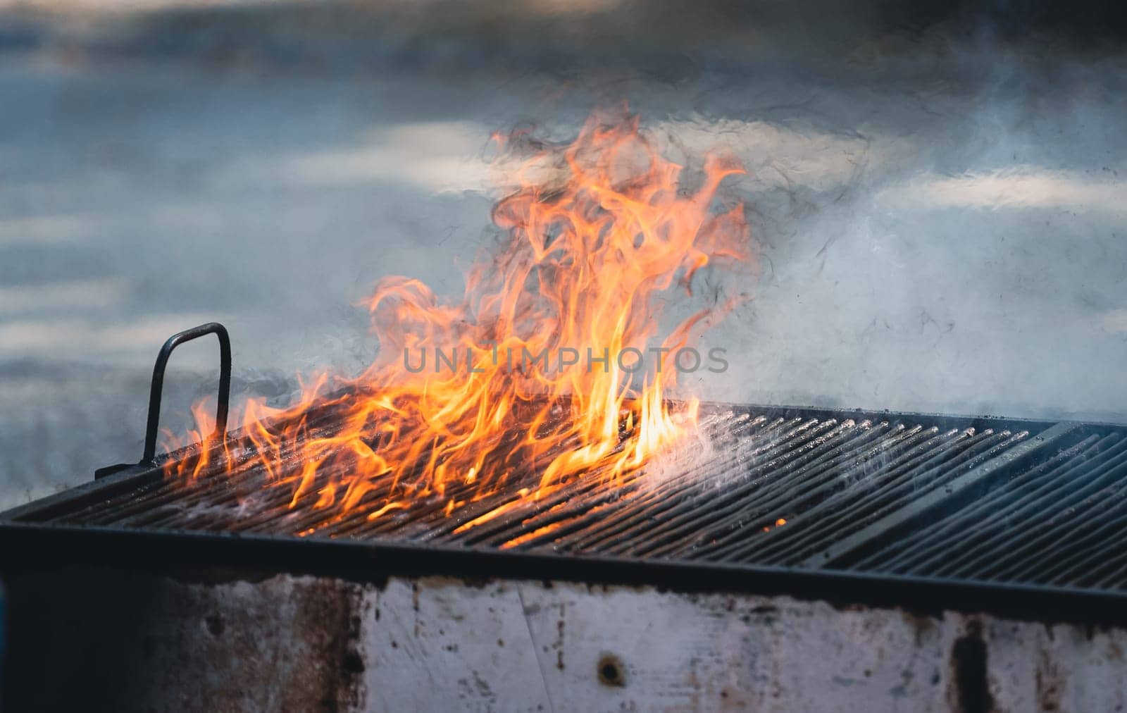 front view of metallic large old barbeque grill with fire flames and smoke coming out