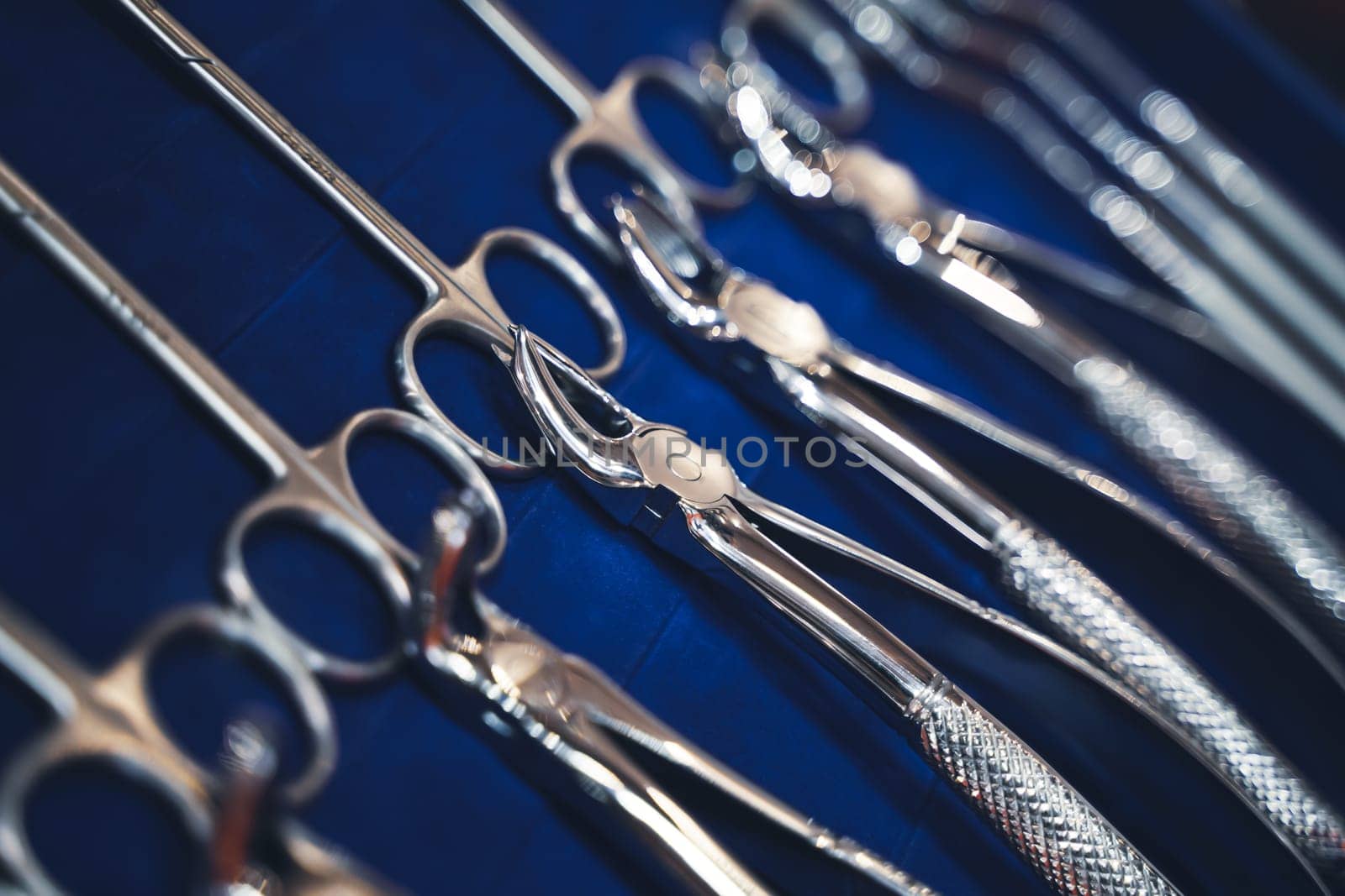 perspective view closeup of row of various steel chrome dental tools on display on blue background with shallow depth of field