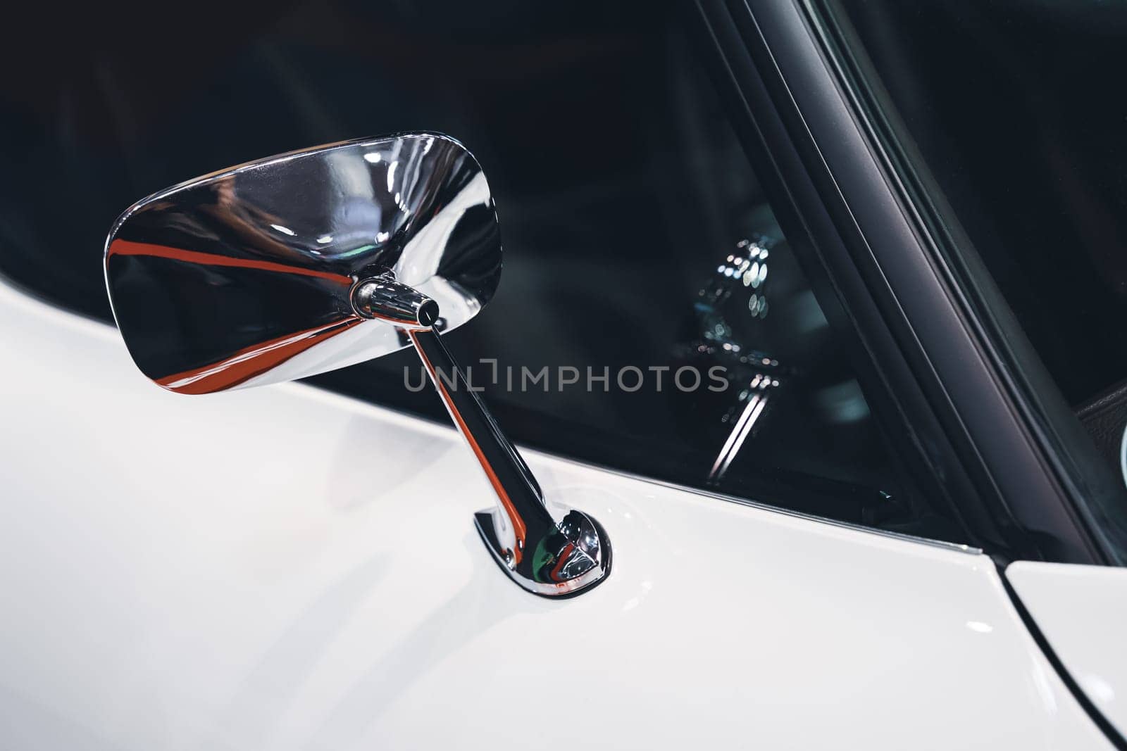 side view detail closeup of chrome rear mirror on white car with classic vintage design