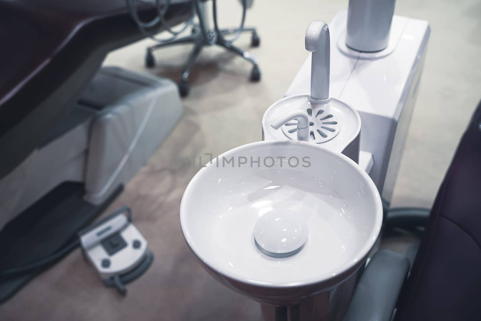 closeup top view of clear dental white ceramic spit sink near chair in dentist office