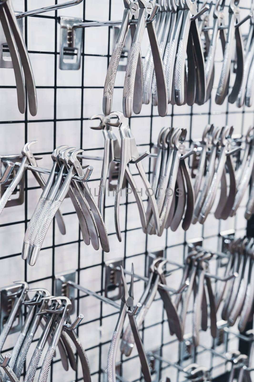 perspective view closeup of row of various stainless steel dental extraction forceps tools hanging on display