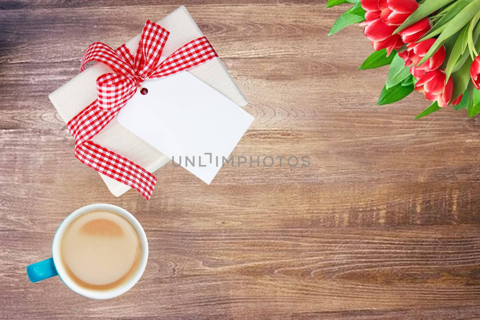 Coffee mug, present box with blank paper tag and tulips on rustic wooden table. Top view. Breakfast on Valentine, Mother or Womens Day. Copy space. Card concept.