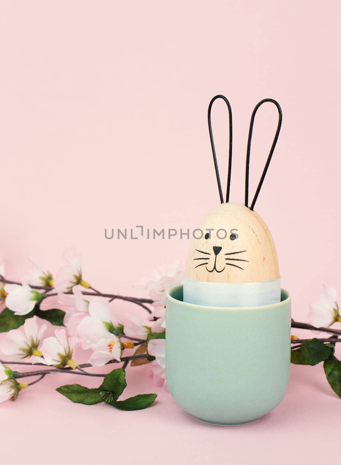 Cute easter bunny or rabbit with a smiling egg face in a cup, spring holiday greeting card with cherry blossoms