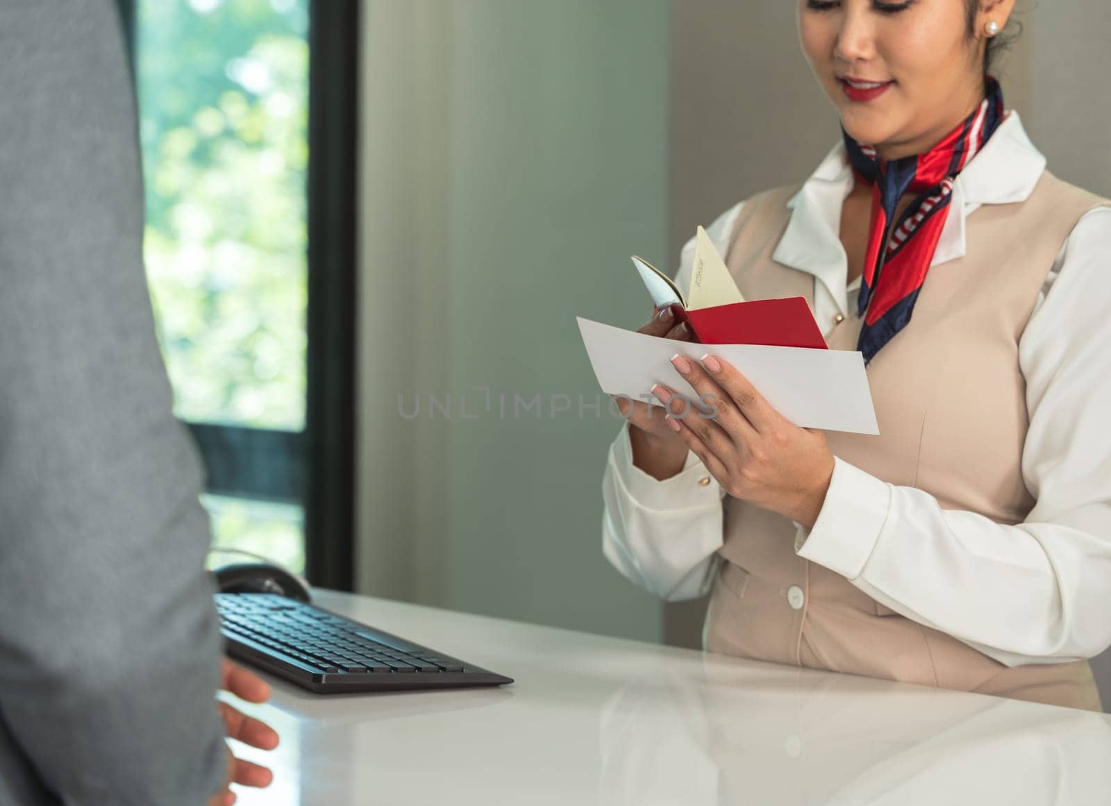 Female flight attendant checking passport and boarding pass at airport terminal counter. Ground staff at departure gate checking travel documents of male passenger