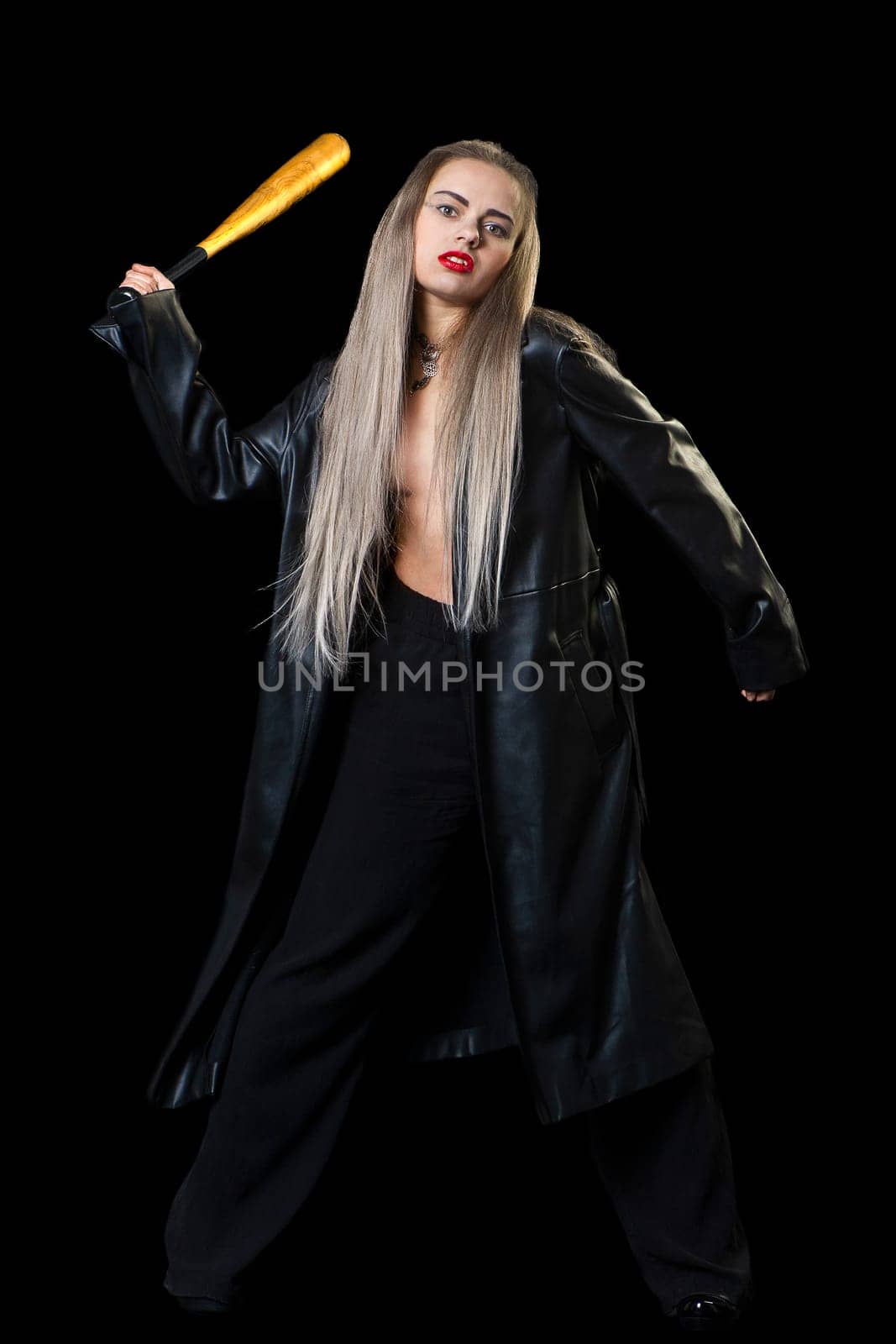 a woman in a black raincoat on a black background with a bat in her hand makes a furious swing. High quality photo
