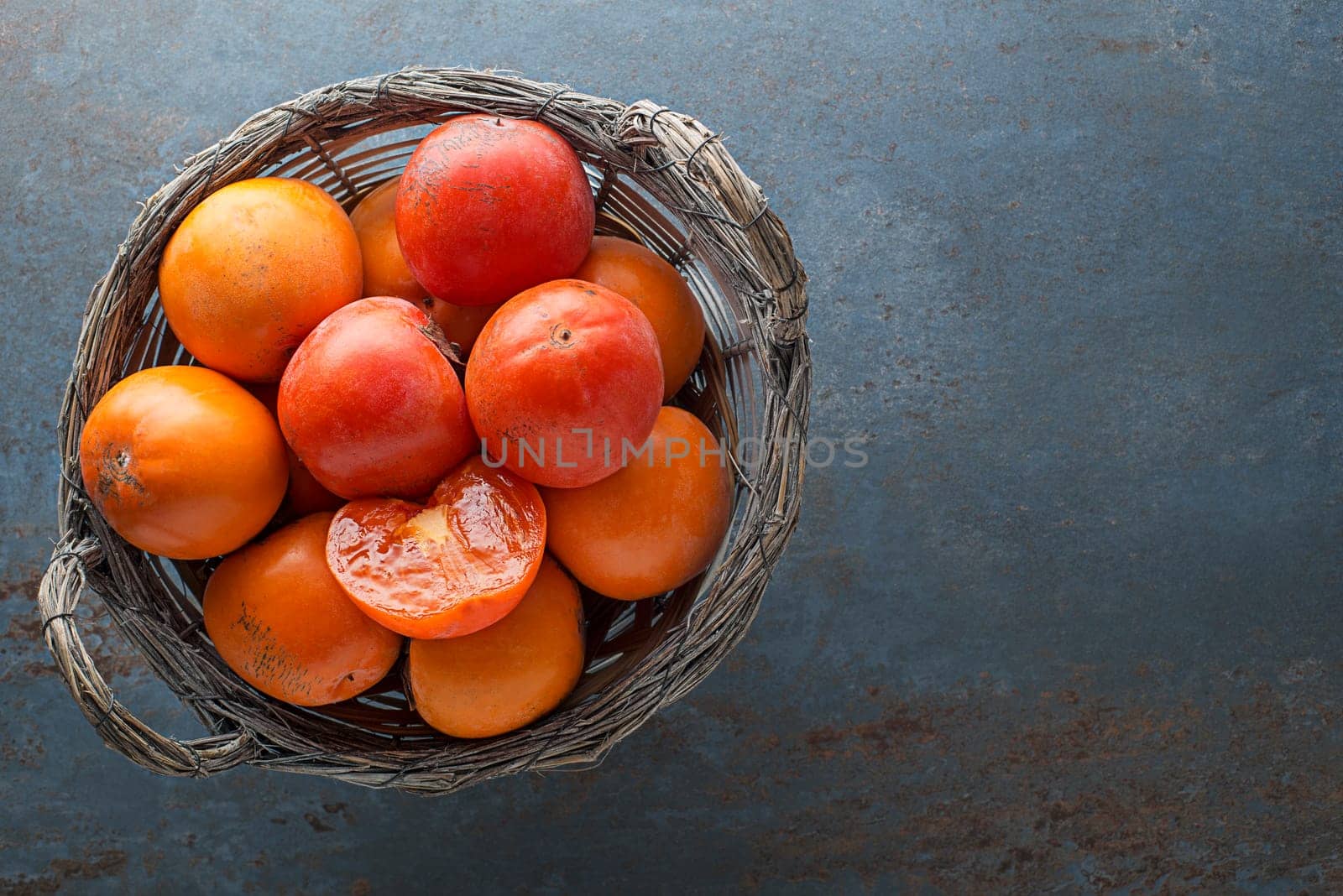 Ripe red and yellow orange persimmon fruit. Close up of fresh kaki in basket on blue table.
