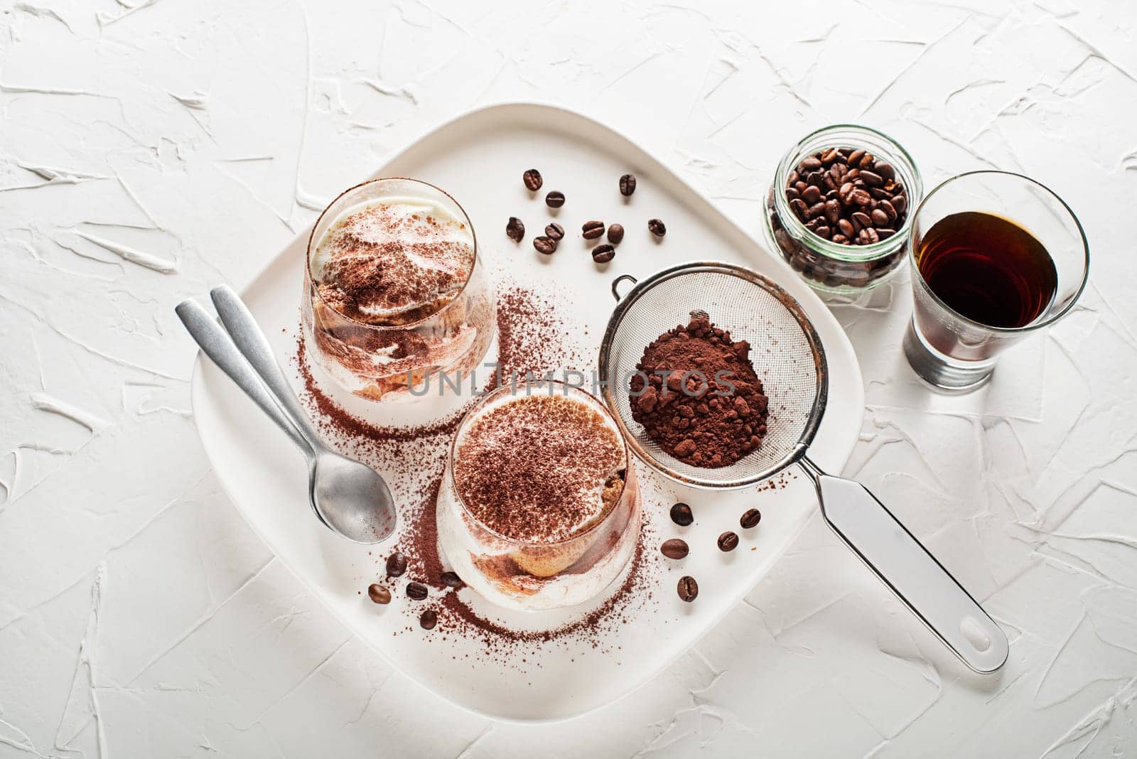 Traditional Italian dessert tiramisu in a glass cup. Homemade tiramisu in glass jars, step by step cooking process. Traditional unbaked italian dessert on white background. Coffee and mascarpone cream cake.