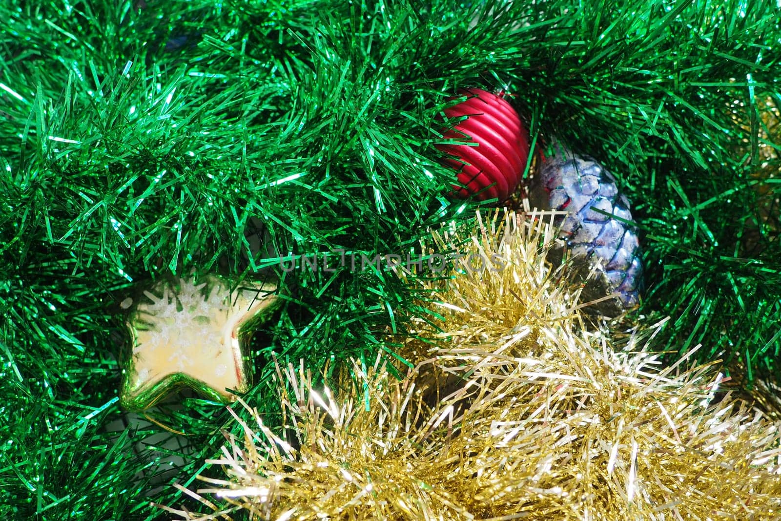 Multi-colored New Year's tinsel and Christmas toys. Green and golden tinsel are intertwined. Christmas decorations. Cone, Christmas ball and star.