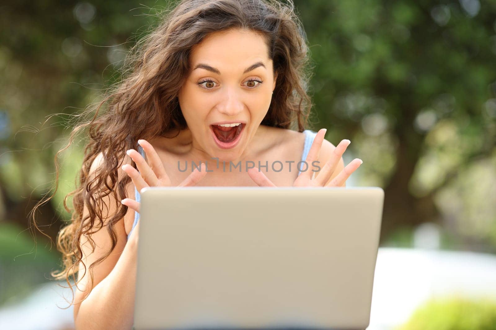 Front view portrait of an amazed woman checking laptop in a park