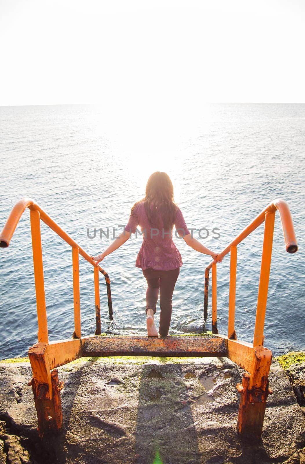 A slender brunette with long hair descends the steps to the sea.