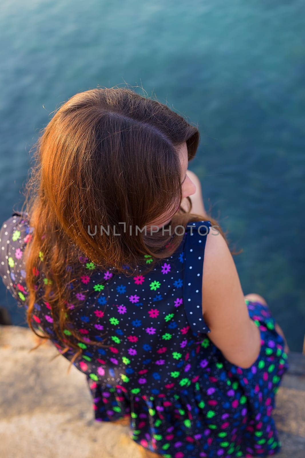 The girl in a beautiful dress is sitting on the pier