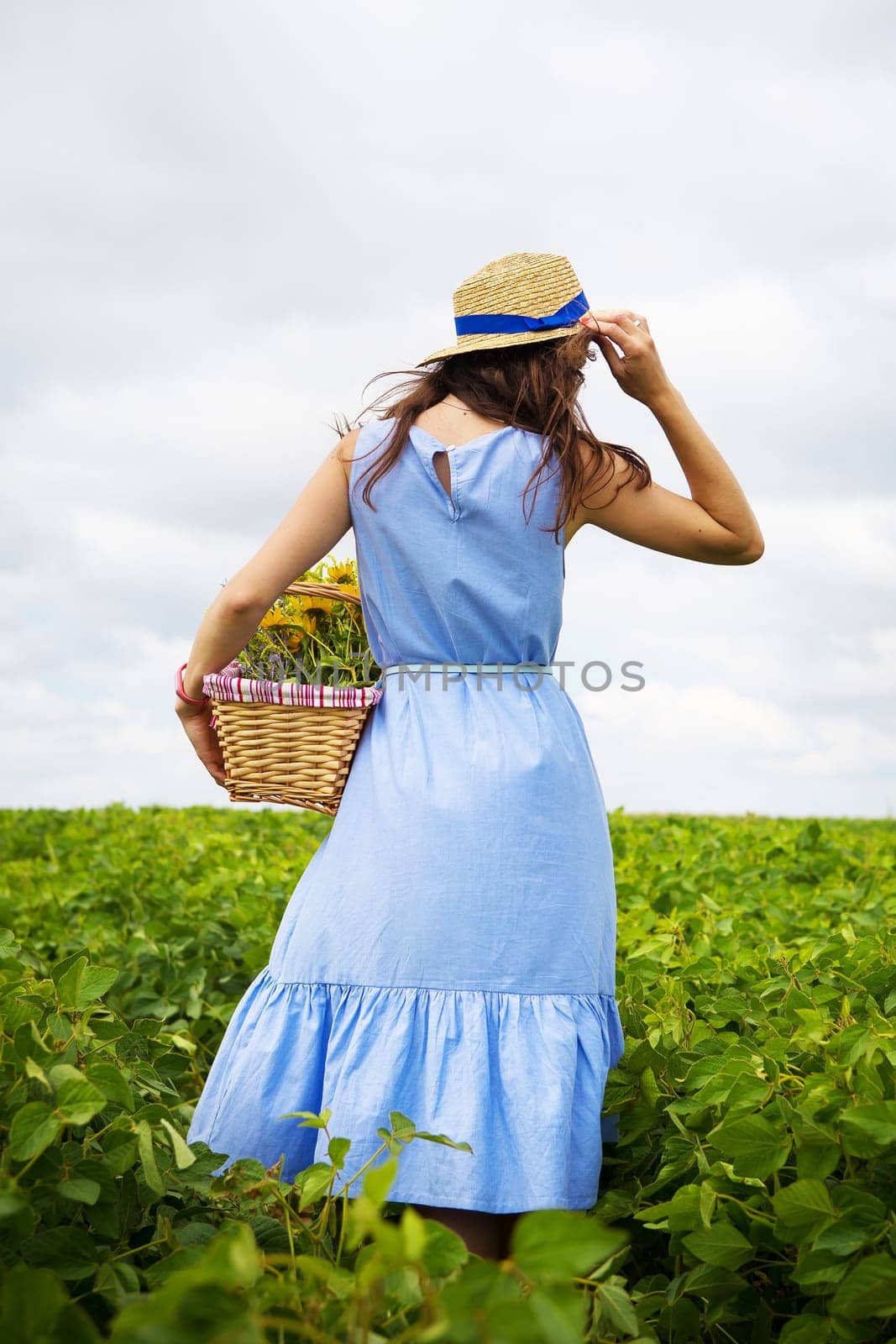 girl in a hat walks on a green field with a basket of flowers.