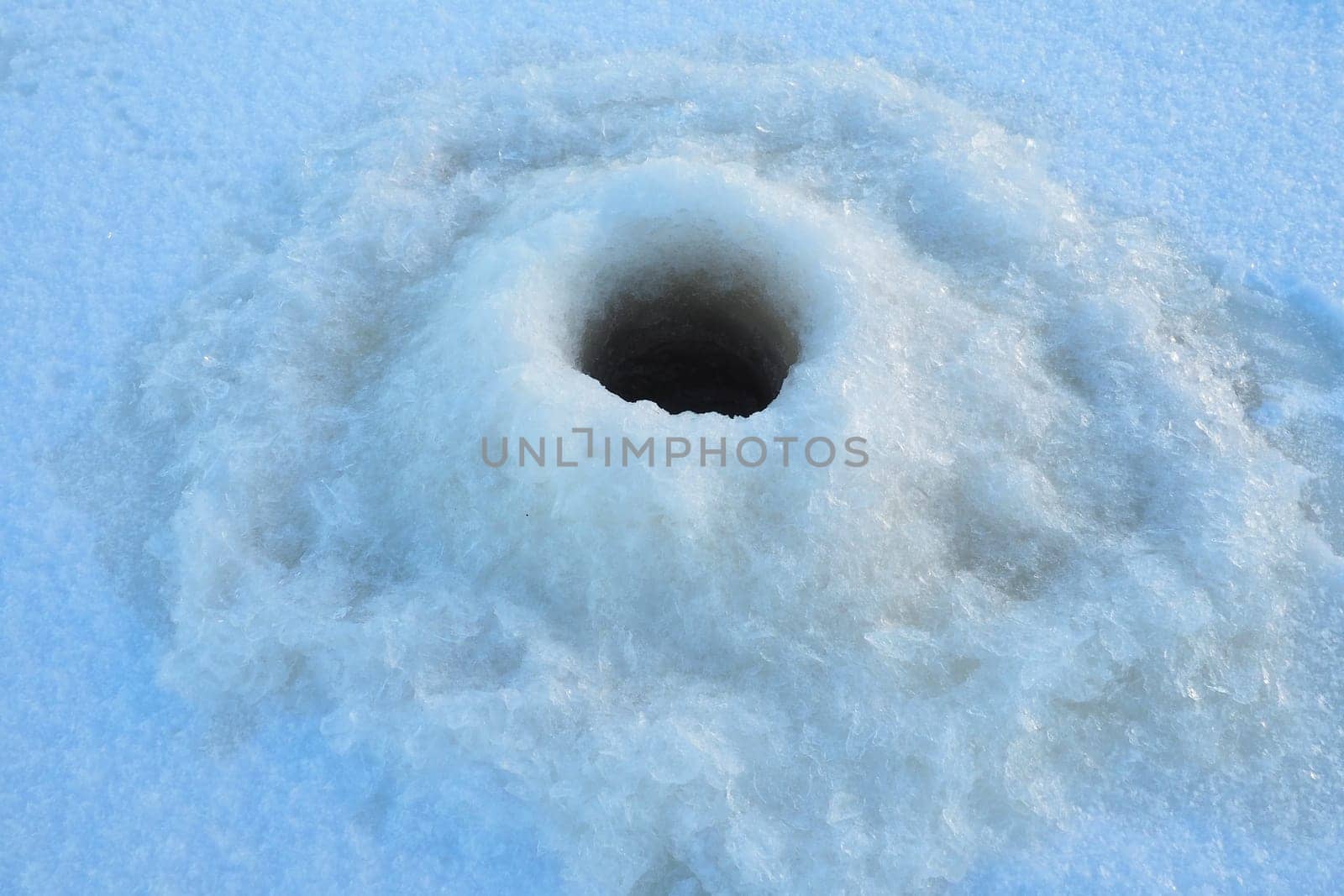 Winter fishing in January. A round hole in the ice and snow, made with an ice pick. Hobby, sports or amateur fishing. Danger of falling into cold water. Brittle ice.