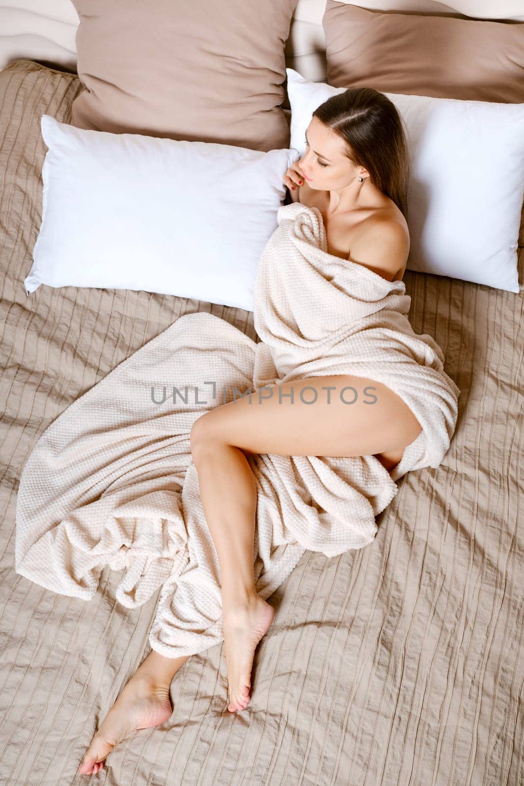 It is time to relax. Attractive fitness woman looking away while lying in bed and wrapping in blanket, top view